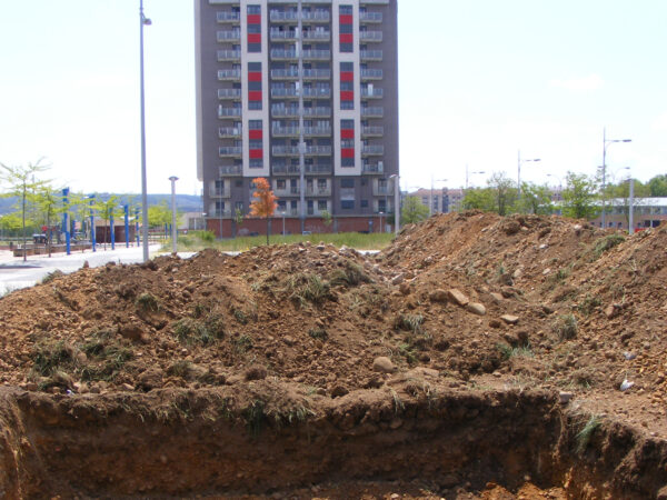 Sondeo arqueológico previo en un sector de nueva urbanización, con edificios residenciales al fondo