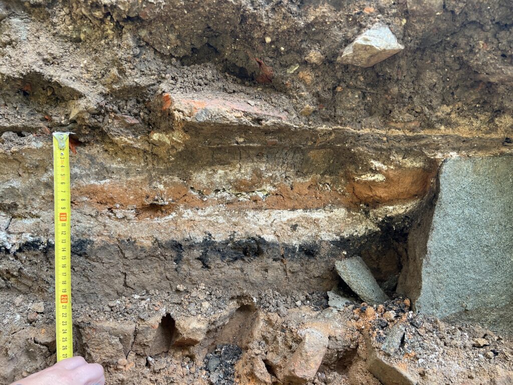 Perfil de excavación con capas de tierra superpuestas de distintas épocas y una cinta métrica como escala